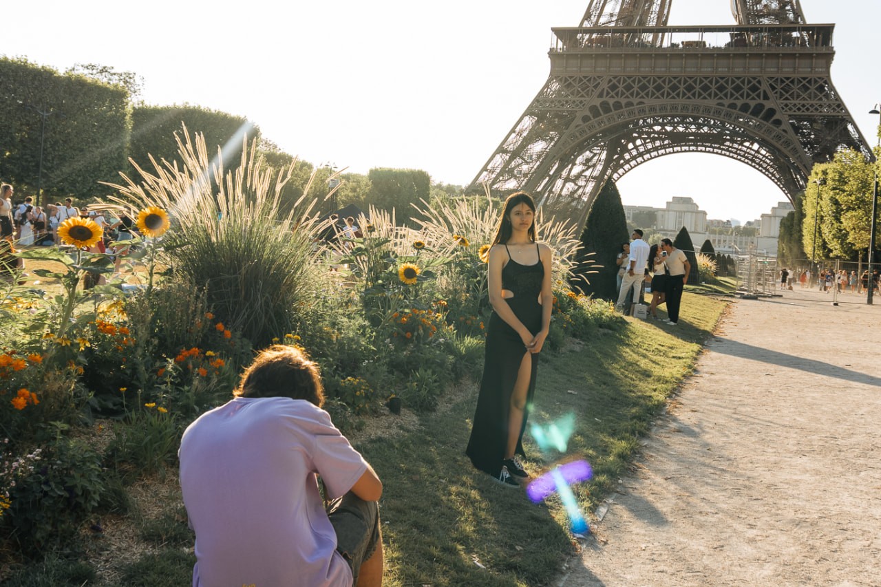 Joven posa junto a un cantero de girasoles con la Torre Eiffel al fondo mientras un integrante del staff la fotografía