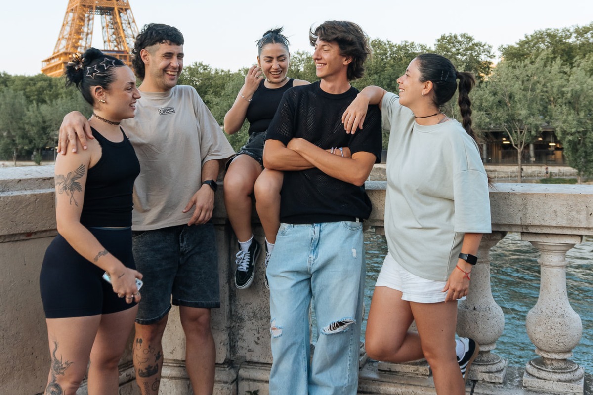 Grupo de adultos riendo y charlando sobre un puente con la Torre Eiffel al fondo