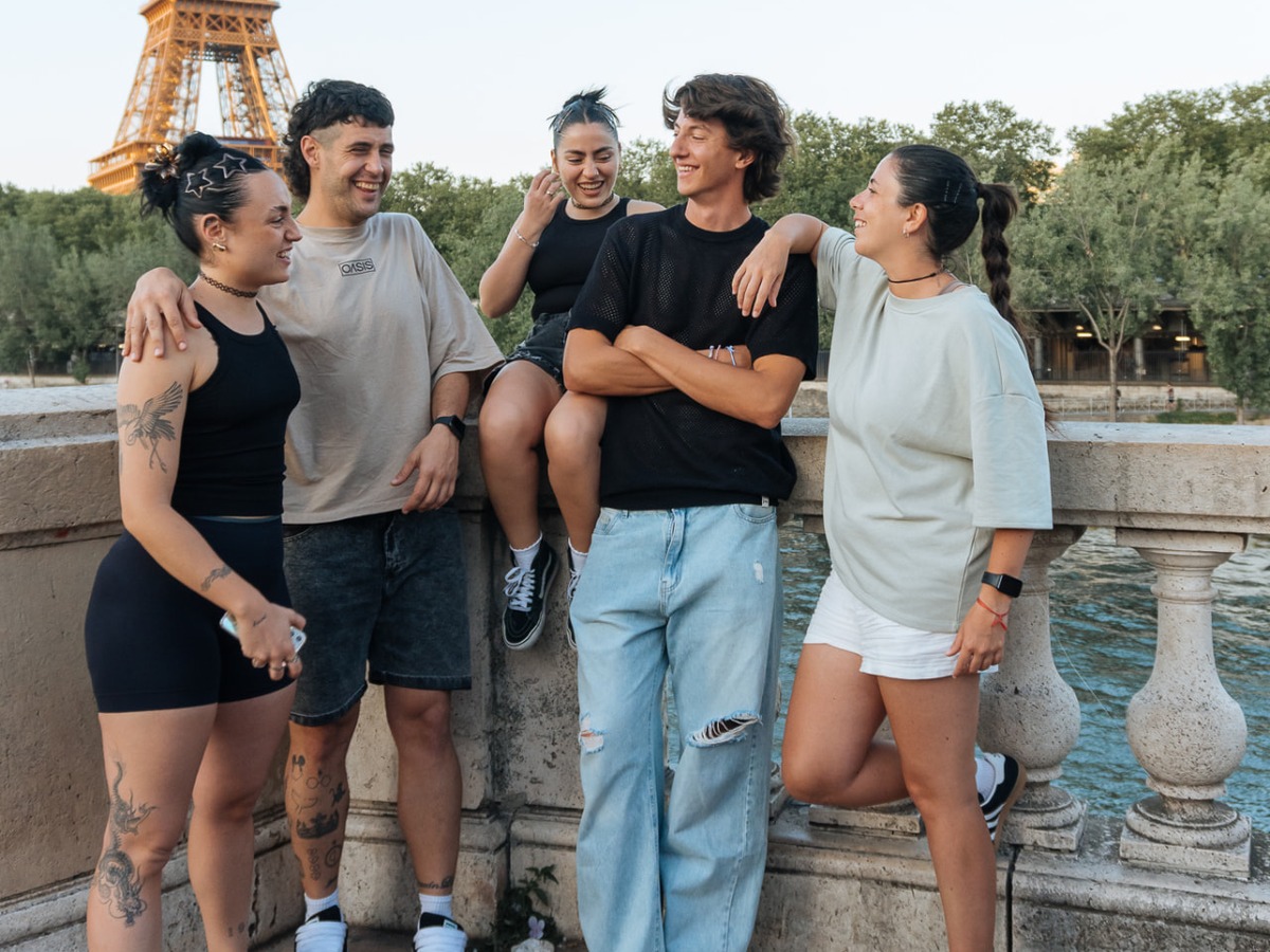 Grupo de adultos riendo y charlando sobre un puente con la Torre Eiffel al fondo